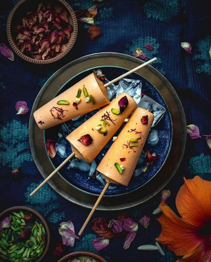 3 kulfis arranged in a plate filled with ice cubes and garnished with dry fruits and rose petals